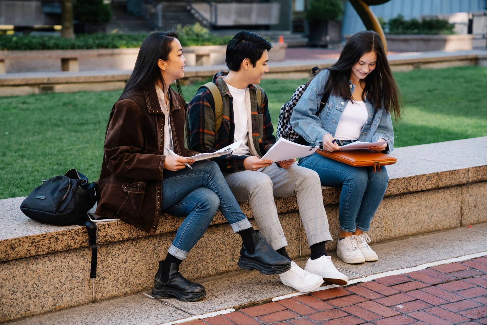 Three students exchanging ideas and reviewing notes outdoors